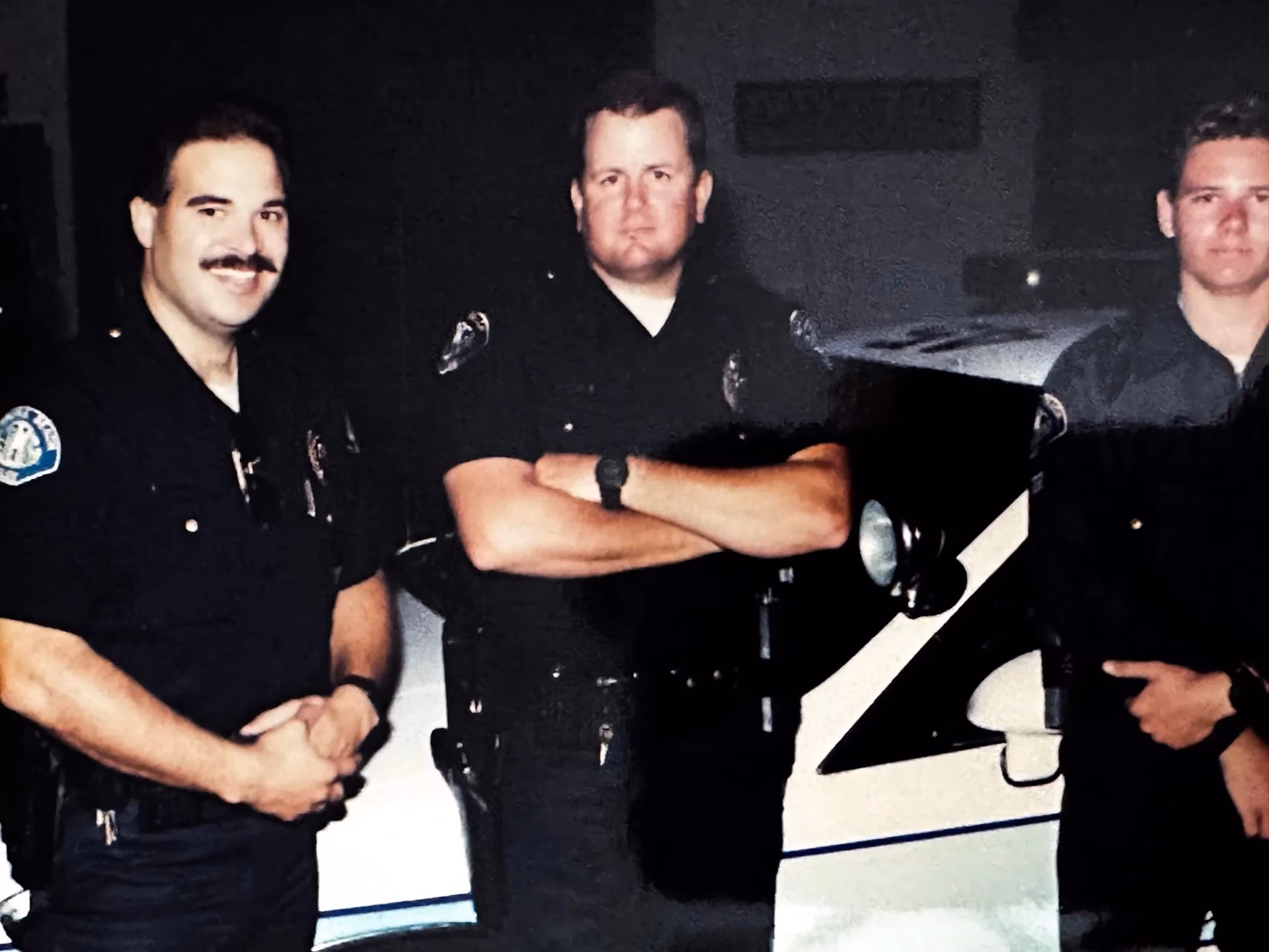 Archival photograph of Officer Fehlman with fellow officers beside a patrol car