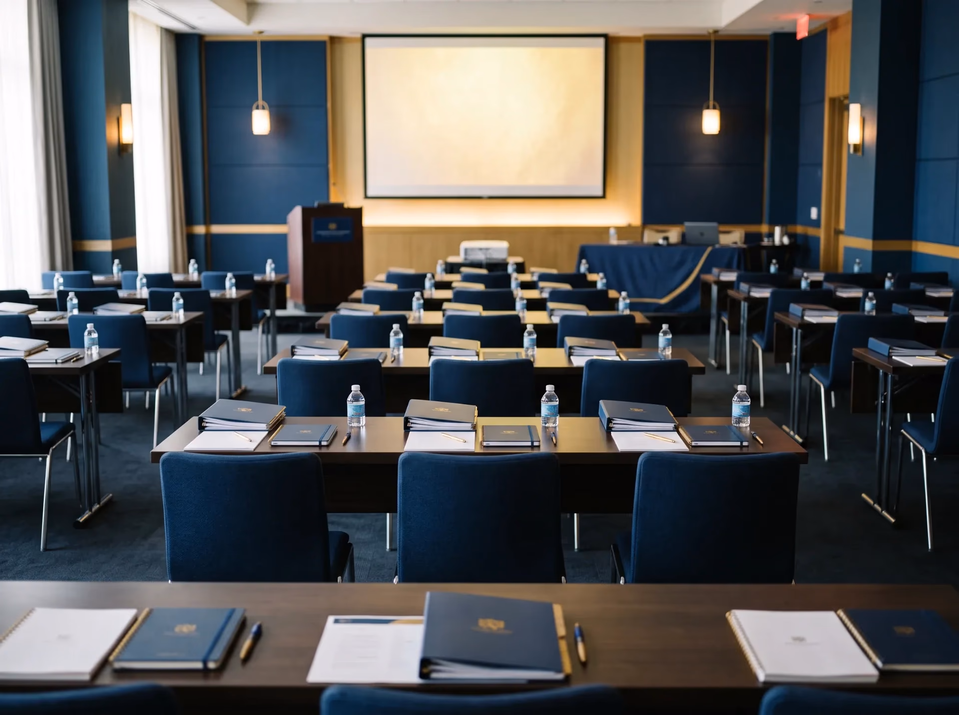 A fully prepared training room seen from the back row, screen lit and handouts squared